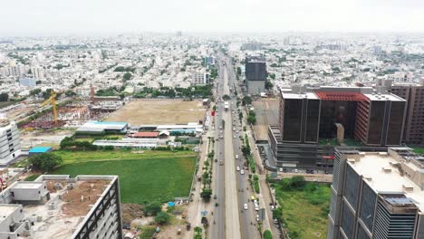 Aerial-cinematic-view-of-Rajkot-city,-lots-of-vehicles-passing-on-the-ring-road,-ground-visible-on-both-sides-of-the-road-and-crores-of-residential-houses-visible-in-the-city