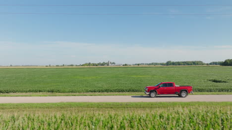 Roter-Pickup,-Der-Mittags-Auf-Einer-Landstraße-In-Der-Nähe-Landwirtschaftlicher-Felder-Fährt