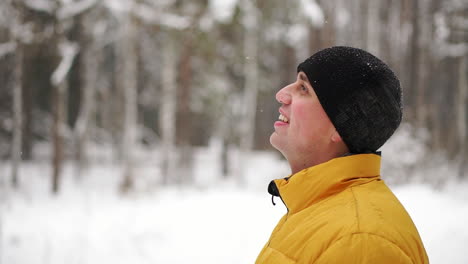 Ein-Mann-In-Einer-Gelben-Jacke-Betrachtet-Den-Schnee-Im-Winter-Im-Wald-Und-Lächelt-In-Zeitlupe