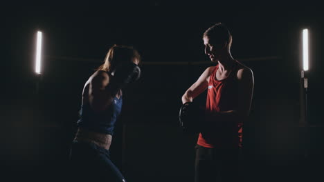 Beautiful-brunette-boxer-working-out-blows-to-the-paws-with-a-trainer-in-a-dark-room