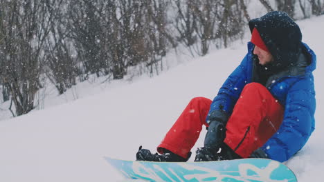 Der-Mann-Sitzt-Im-Schnee-Mit-Reißverschlussstiefeln-Und-Snowboard