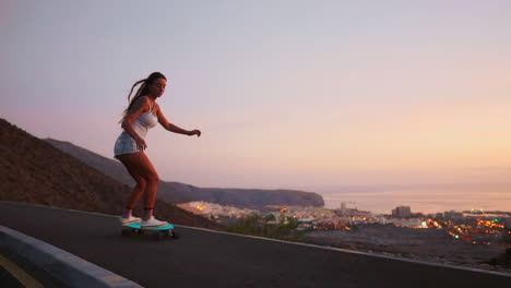 In-slow-motion,-a-breathtaking-young-skateboarder,-dressed-stylishly-in-shorts,-rides-her-board-along-a-mountain-road-at-sunset,-capturing-the-mountains'-captivating-view
