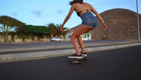 Against-the-backdrop-of-mountains-and-a-beautiful-sky,-a-woman-engages-in-slow-motion-skateboarding-on-a-road-at-sunset.-She-wears-shorts