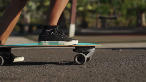 Slow-motion-captures-the-essence-of-summer-as-a-young-woman-rides-a-longboard-near-palm-trees,-donning-shorts-and-sneakers