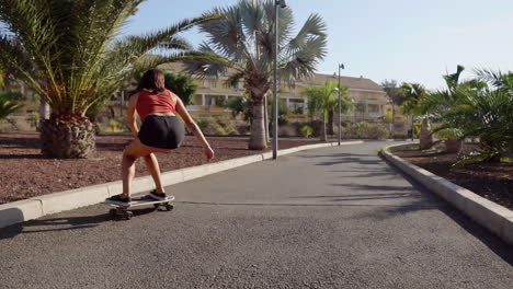 Slow-motion-portrays-a-mesmerizing-scene:-a-young-girl-skillfully-riding-her-longboard-by-the-beach-and-palm-trees