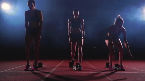 Young-female-runner-athlete-with-smartwatch-ready-to-sprint-at-running-track-starting-line