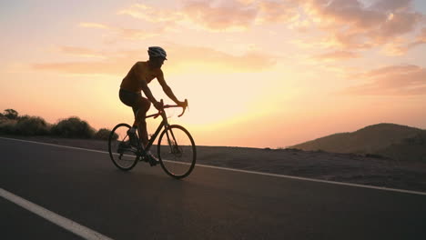 Slow-motion-captures-the-athlete-cycling-along-a-mountain-serpentine-on-a-bike,-taking-in-the-island's-view,-embodying-dedication-to-a-healthy-lifestyle-at-sunset