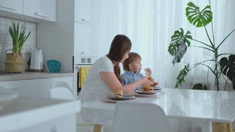 Mama-Hilft-Ihrem-Kleinen-Sohn,-In-Der-Küche-Einen-Burger-Zu-Essen