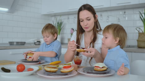 Beautiful-young-mother-with-two-children-sons-on-white-light-kuna-cook-with-burgers