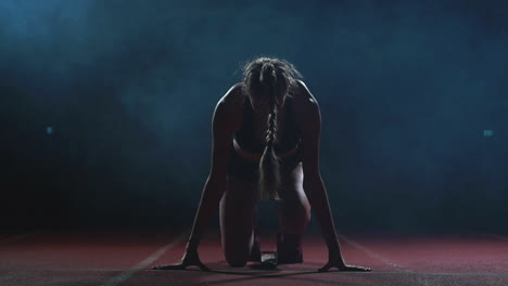 Professional-woman-athlete-on-a-dark-background-gotovtes-to-run-the-sprint-of-Jogging-shoes-in-sneakers-on-the-track-of-the-stadium-on-a-dark-background.-Close-up