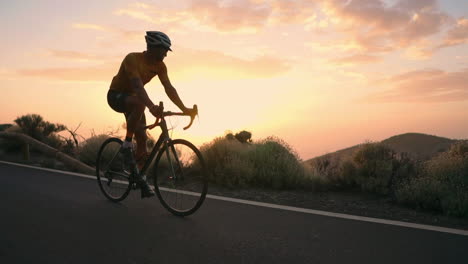 The-athlete-on-a-bike-is-seen-in-slow-motion-conquering-a-mountain-serpentine,-cherishing-the-island's-view,-epitomizing-a-devotion-to-a-healthy-lifestyle-at-sunset