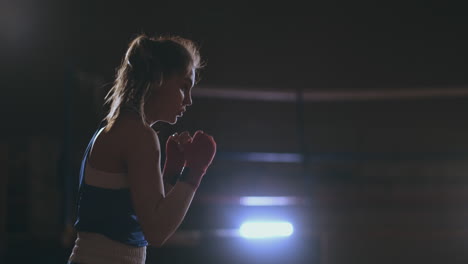 A-beautiful-woman-conducts-a-shadow-fight-practicing-technique-and-speed-of-strikes-while-training-hard-for-future-victories.-Dark-gym-background.-steadicam-shot