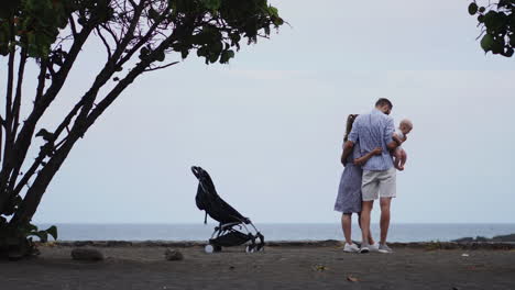 With-the-sunshine-illuminating-their-path,-a-content-young-Caucasian-family,-including-their-one-year-old-son-in-a-stroller,-leisurely-walks-along-a-wooden-jetty