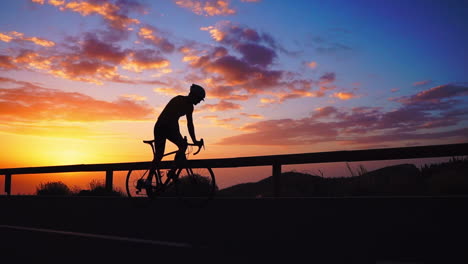 Silhouette-In-slow-motion,-the-athlete-cycles-on-a-mountain-serpentine,-embracing-the-island's-view,-symbolizing-a-dedication-to-a-healthy-lifestyle-during-sunset