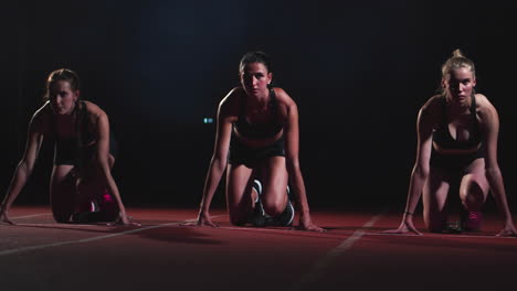 Drei-Sportlerinnen-Starten-Nachts-Auf-Dem-Laufband-Aus-Sitzender-Position-Zum-Rennen-Auf-Der-Sprintdistanz