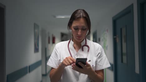 Fröhlicher-Kinderarzt-Benutzt-Smartphone-Im-Krankenhausflur