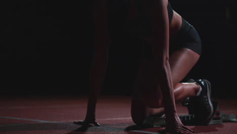 Professional-woman-athlete-on-a-dark-background-gotovtes-to-run-the-sprint-of-Jogging-shoes-in-sneakers-on-the-track-of-the-stadium-on-a-dark-background.-Close-up