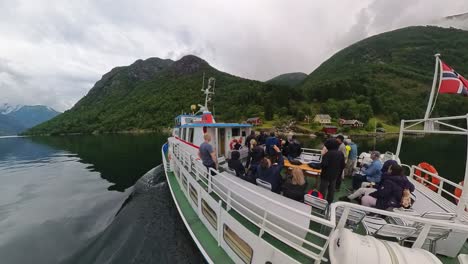 Ein-Touristenboot-Fährt-An-Einer-Kleinen,-Abgelegenen-Siedlung-Ohne-Straße-Im-Norwegischen-Fjærlandsfjord-Vorbei-–-Handgehaltener-Weitwinkel,-Der-Sowohl-Das-Boot-Mit-Touristen-Als-Auch-Die-Kleine-Siedlung-Im-Hintergrund-Zeigt