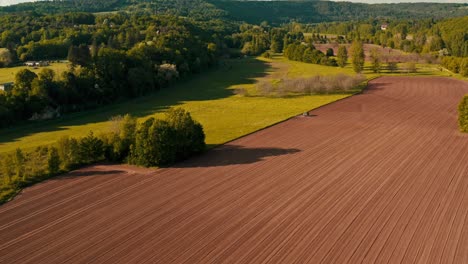 Planting-soil-tilled-and-agitated-preparing-for-growing-season-in-lush-valley,-aerial