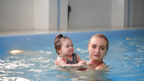 Young-mom-in-the-pool-playing-with-her-baby-daughter-in-slow-motion.-Sports-family-engaged-in-an-active-lifestyle