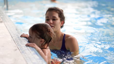Beautiful-mother-teaching-cute-baby-girl-how-to-swim-in-a-swimming-pool.-Child-having-fun-in-water-with-mom.