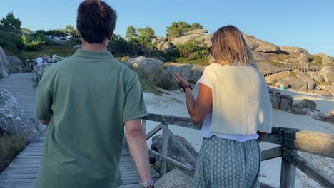 Caucasian-young-couple-walking-through-beach-promenade-at-sunset-in-summer