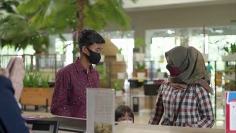 Young-family-and-receptionist-at-counter-in-hotel-wearing-medical-masks-as-a-precaution-against-the-virus