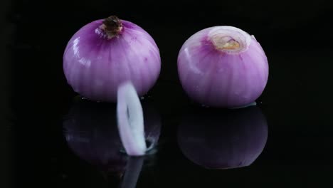 Cinematic-footage-of-an-onion-slice-being-tossed-on-onion-sitting-on-a-reflective-surface-in-slow-motion-played-in-reverse,-Slomo