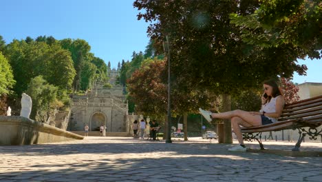 Schöne-Frau,-Die-Am-Telefon-Spricht-Und-Auf-Einer-Bank-Im-Heiligtum-Nossa-Senhora-Dos-Remediso-In-Lamego,-Portugal,-Sitzt