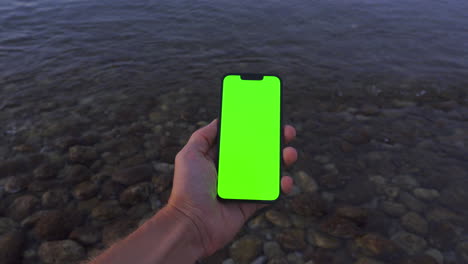 Golden-Hour-POV:-Hand-Holding-iPhone-14-with-Green-screen-by-Rocky-Calm-Sea,-Chroma-Key