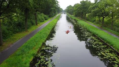 Aerial-view-of-people-kayakking-in-beautiful-green-environment,-canal-filled-with-water-lilies