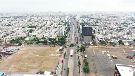 Aerial-cinematic-view-of-Rajkot-city,-lots-of-vehicles-passing-on-the-ring-road,-ground-visible-on-both-sides-of-the-road-and-crores-of-residential-houses-visible-in-the-city