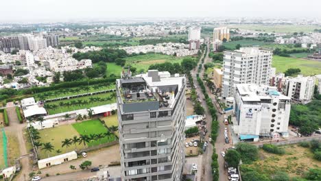 Aerial-view-of-Rajkot-City's-Skyscraper-Building,-camera-panning-from-bottom-to-top-showing-entire-building-with-terrace-garden-restaurant-on-top-floor,-Synergy-Hospital-also-visible