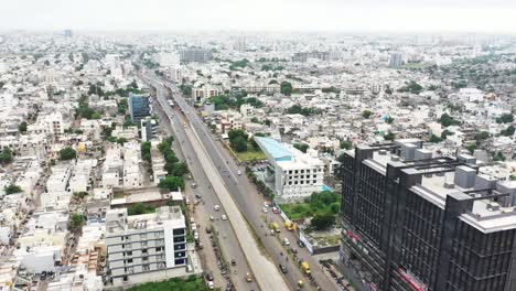 Aerial-cinematic-view-of-Rajkot-city-showing-vehicles-passing-over-live-over-bridge-on-ring-road,-millions-of-low-rise-residential-buildings,-highrise-commercial-and-residential-buildings-in-the-city