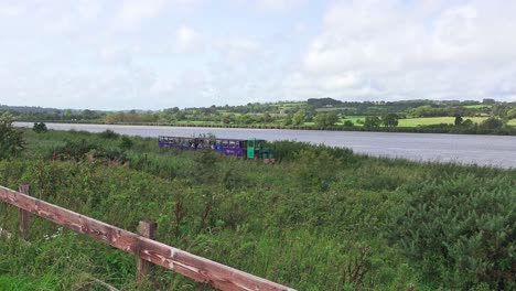 Tren-Turístico-Pasando-Con-El-Río-En-El-Fondo-En-Waterford-Greenway-Irlanda-En-Un-Cálido-Día-De-Verano