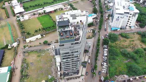 Aerial-view-of-Rajkot-City's-Skyscraper-Building-with-camera-panning-down-to-the-top-and-surrounding-scene-with-cars-passing-by-and-the-ground-looking-completely-empty