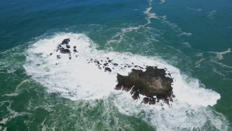 Orbit-drone-shot-of-powerful-waves-crashing-on-coral-rock