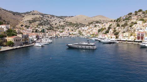 Large-luxurious-super-yacht-in-the-port-of-Symi-in-Greece,-aerial-backward