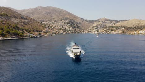 Front-view-of-a-luxurious-mega-yacht-leaving-the-bay-of-Symi-in-Greece,-drone