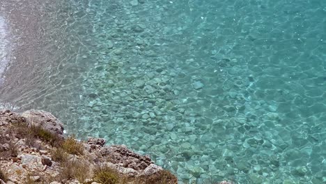 Quiet-bay-on-Mediterranean-seaside-with-the-beautiful-beach-and-cliffs-over-turquoise-clean-sea-water