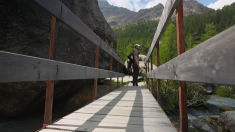 Hiker-With-Backpack-Walking-On-The-Wooden-Bridge-To-The-Alpe-Ventina-In-Valmalenco,-Sondrio,-Italy