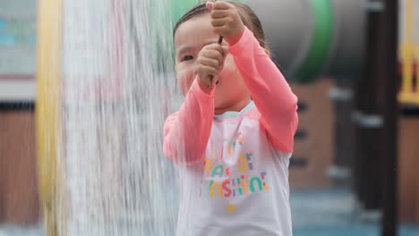 Face-of-Happy-Smiling-Little-Girl-Dragging-Wire-to-Initiate-Water-Shower,-Mother-Holds-Bare-Foot-Leg-Under-Pouring-Water-Splashing-It-Around-in-Slow-motion