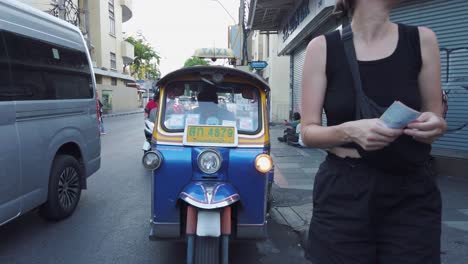Caucasian-tourist-woman-pays-tuk-tuk-taxi-driver-on-Bangkok-street