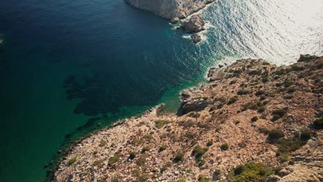 Drone-descends-and-tilts-up-to-reveal-white-grey-rocky-islands-protecting-bay-on-syros-greece