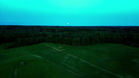 Disparo-Aéreo-De-Drones-Con-Superluna-Elevándose-Sobre-Un-Paisaje-Forestal-En-Letonia-Durante-La-Hora-Azul