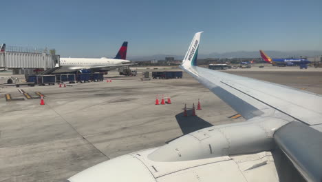 Panorámica-Desde-El-Motor-Del-Avión-Westjet-737-Hasta-El-Ala,-Mientras-Está-Estacionado-En-Un-Aeropuerto-Relajado-Con-Otros-Aviones-Al-Fondo,-Desde-El-Punto-De-Vista-De-Un-Asiento-Junto-A-La-Ventana,-El-13/7/2023