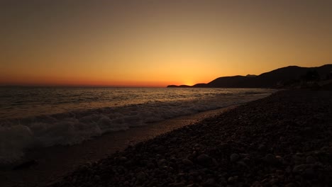 Static-shot-of-sea-waves-splashing-on-pebbles-beach-at-dramatic-sunset,-burning-sky-and-shining-golden-waves-on-beautiful-bay-in-Mediterranean
