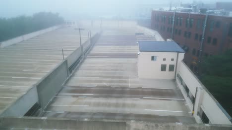 Aerial-descending-dolly-along-parking-garage-ramp-leading-to-upper-level-on-foggy-misty-morning