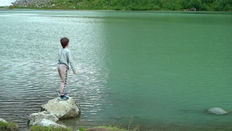 Boy-throwing-a-rock-into-green-glacial-lake-during-trip-to-Boyabreen-glacier-in-Norway---Slow-motion