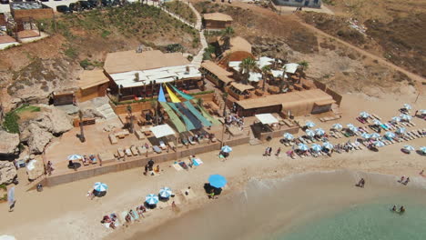 Drone-Pilot-Sitting-On-Lounge-Chair-In-The-Beach-Flew-The-Drone-Camera-Away-From-Him-To-Reveal-Scenic-Beach